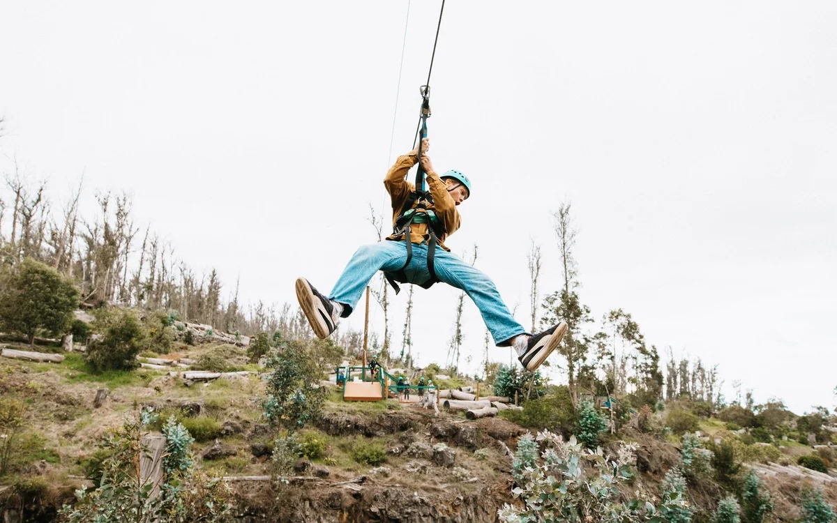 A rider crossing on a zip-line high above green Upcountry pasture on Maui