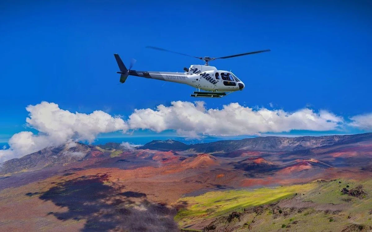 A helicopter flying above the green ridges and valleys of east Maui