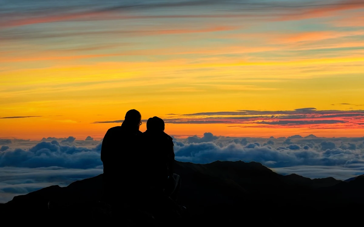 Visitors standing at the summit rail of Haleakala watching the sky lighten at dawn