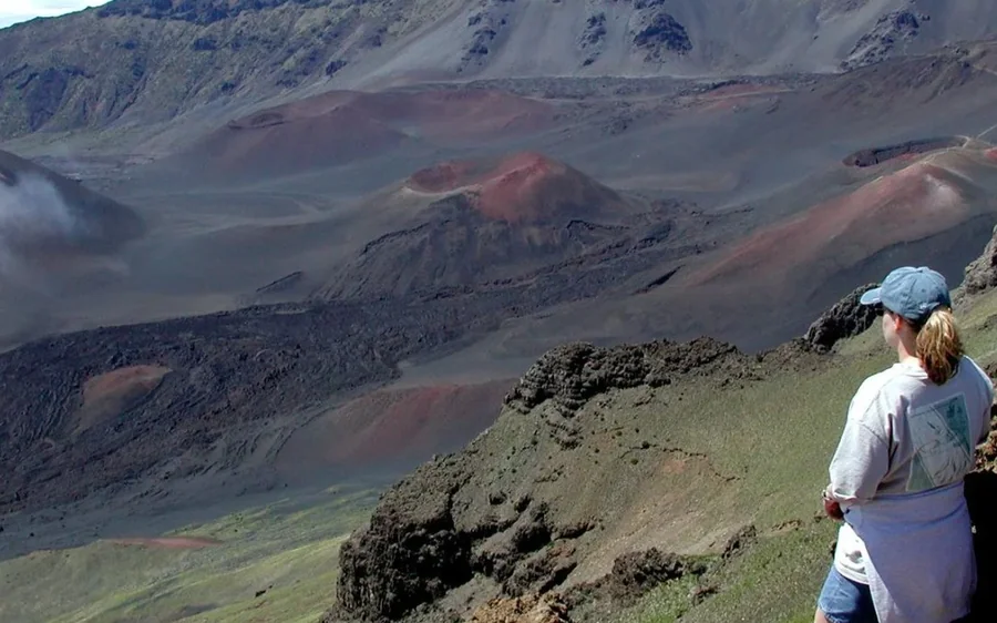 A walker in a cap standing on the crater rim above the wide red crater floor