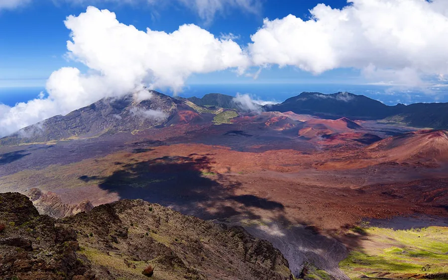 A white helicopter in flight over dark lava ground with cloud behind it