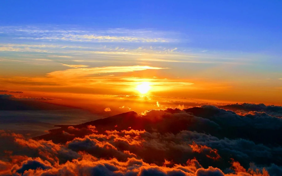 The sun low over a solid layer of cloud seen from the summit, the sky orange above it
