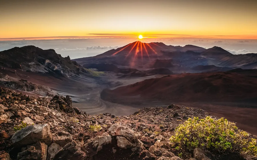 The sun coming up over the rim of the crater with red cinder slopes in front