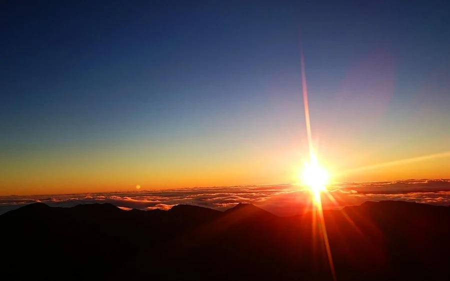 A bright sunburst low on the horizon with the land still in shadow